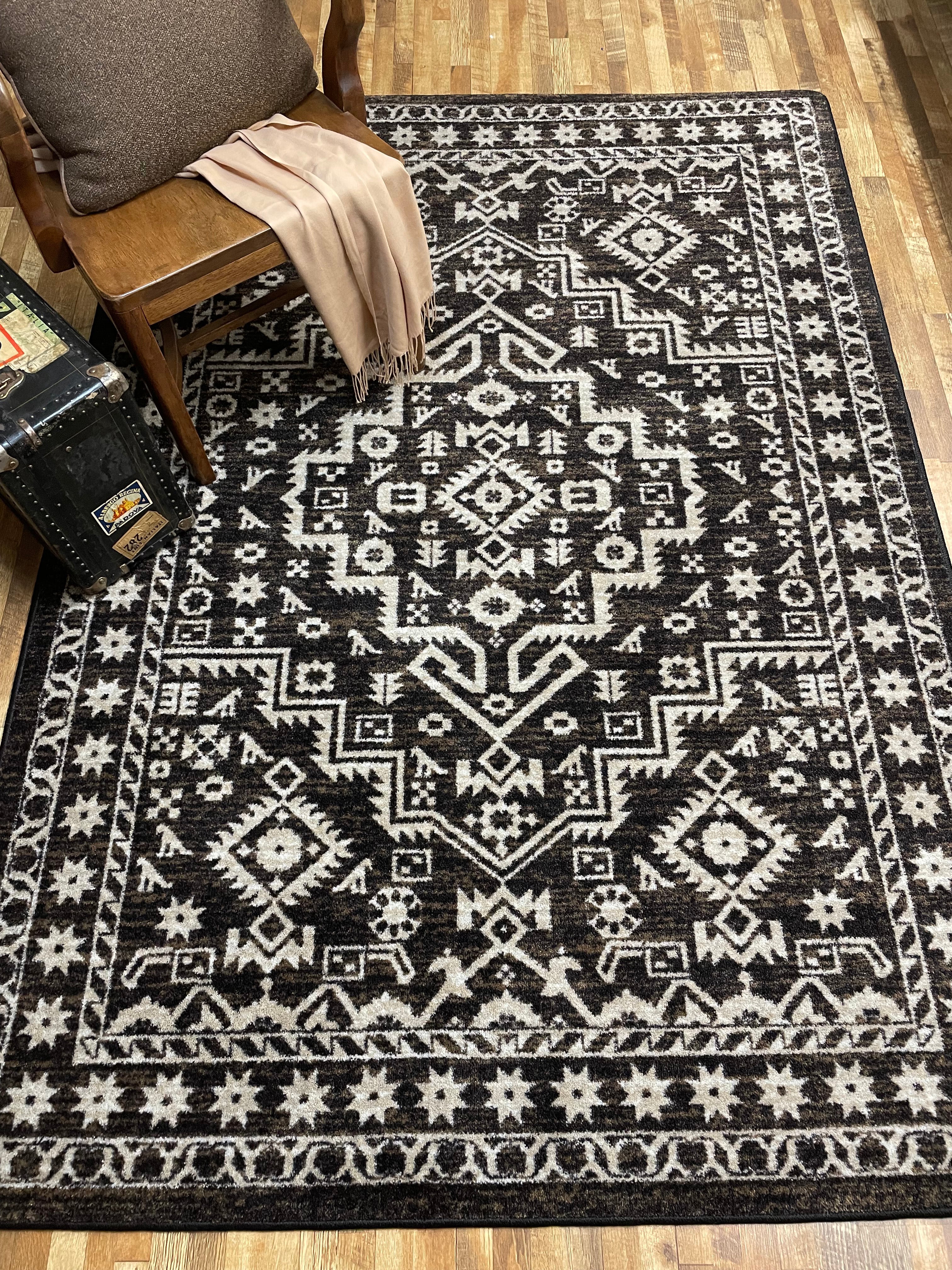 Patterned black and white rug on a wooden floor with a chair and suitcase.