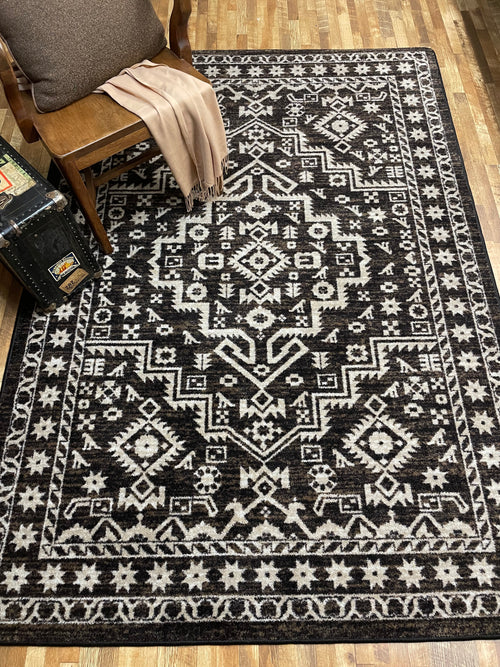 Patterned black and white rug on a wooden floor with a chair and suitcase.